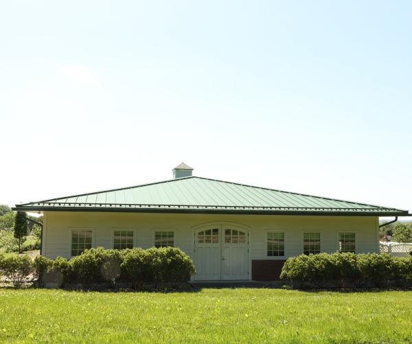 The Dawes Arboretum's physical archive sits under the sun among green grass and green shrubs. The building has a green roof and white siding.