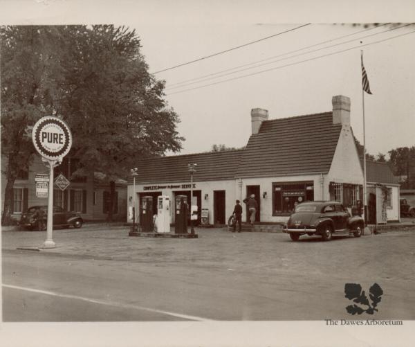 A black and white photo of a Pure Oil gas station is alongside the raod near a Pure Oil gas station sign.