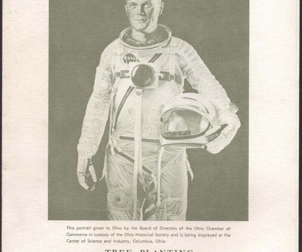 This is a black and white piece of history, specifically, it is the portrait of John Glenn's tree planting. He is standing in his astronaut's uniform and holding his helmet. It reads: "Colonel John Herschel Glenn Jr." 