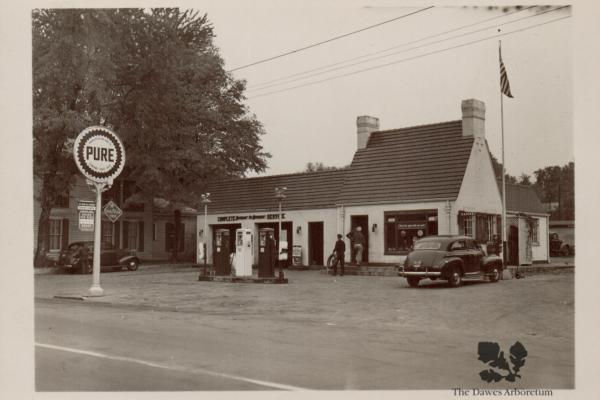 This is a photo of a Pure Oil station. It is a balck and white station with the Pure Oil sign out in front of it. Trees are behind the station.