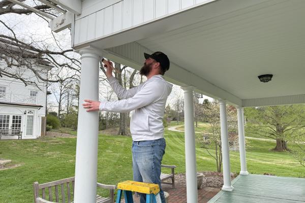 A Dawes employee wearing a white shirt and blue jeans paints The Dawes Arboretum's History Center white.