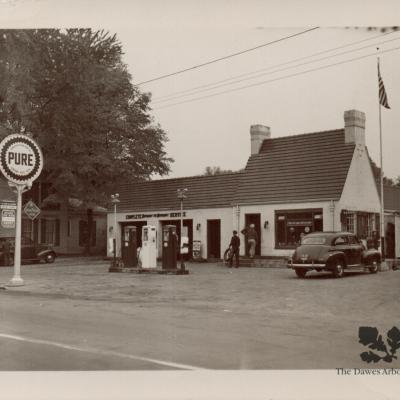 A black and white photo of a Pure Oil gas station is alongside the raod near a Pure Oil gas station sign.